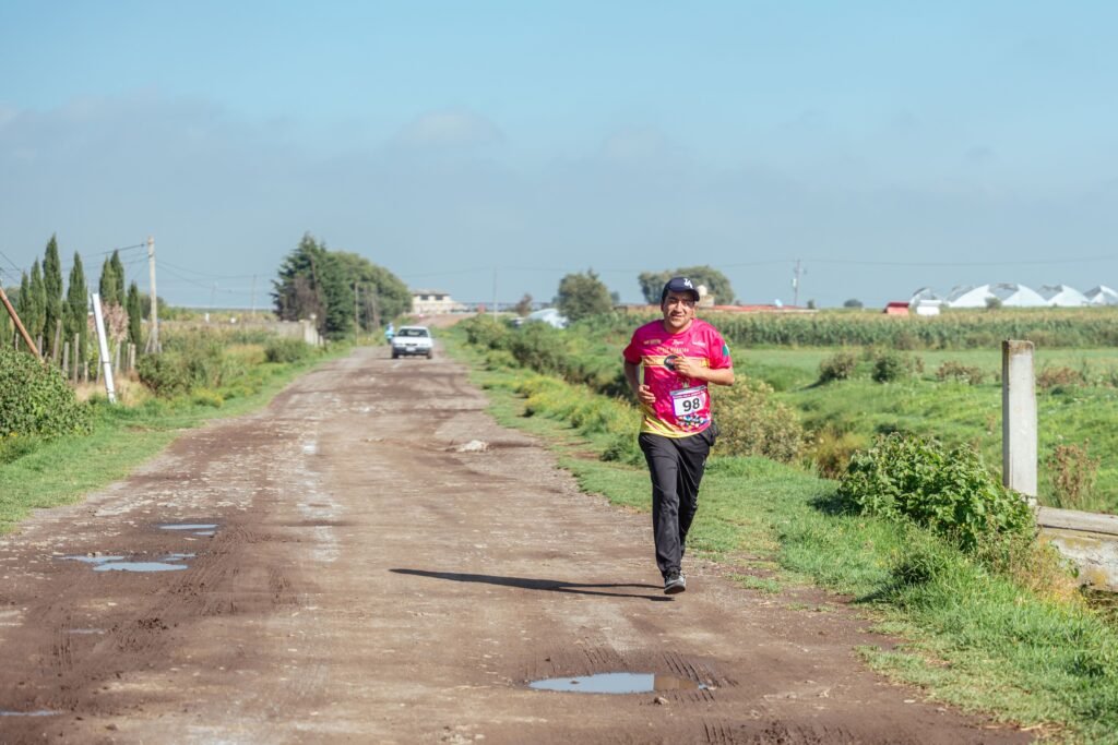 A man jogs on a rural dirt road, enjoying a sunny day in the countryside.