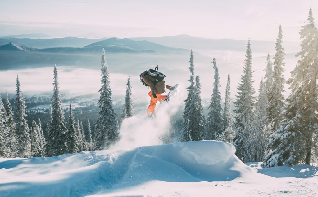 Dynamic shot of a snowboarder mid-air amidst snowy trees and mountains in winter.